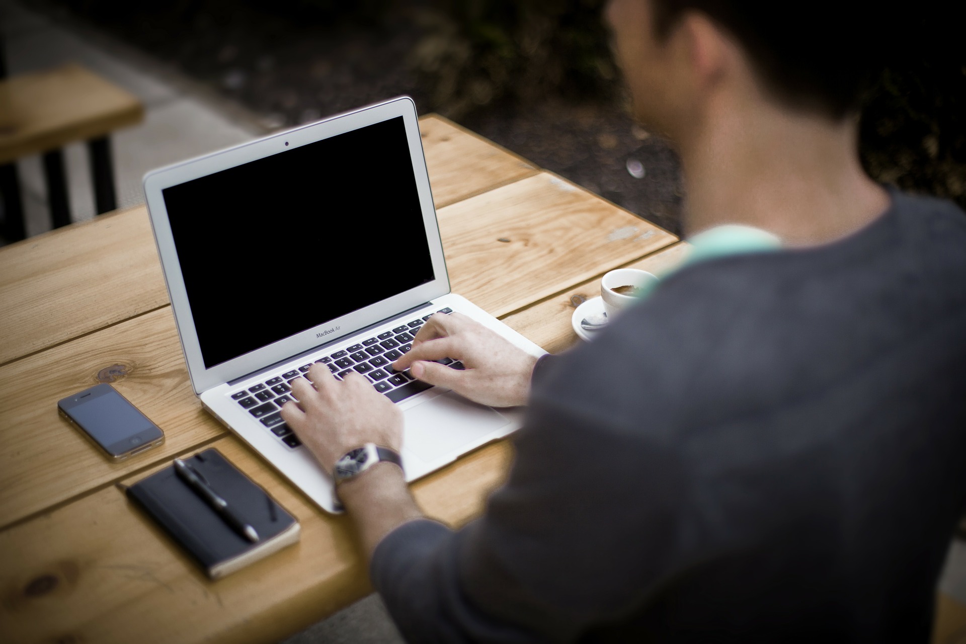 A person typing on a laptop whilst sat at a wooden table